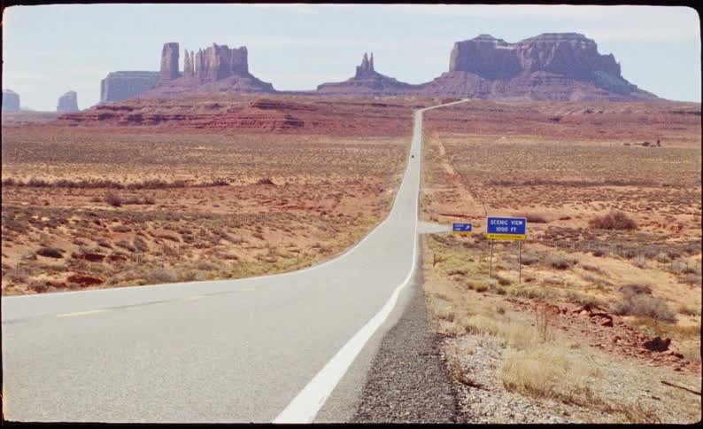 The long asphalt road creates a stark vertical line that draws the eye directly toward the horizon it starts wide at the bottom of the frame and tapers significantly as it stretches into the distance emphasizing the vast scale of the desert
