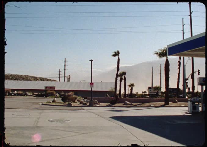 A gas station on the side of the street with cars driving by on a sunny day