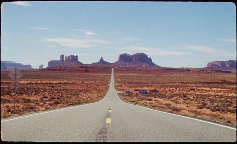 A long straight highway stretching toward the iconic red rock buttes of monument valley under a clear sky