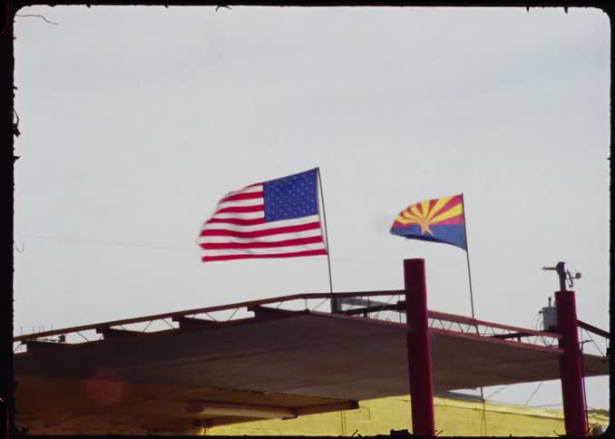 United states and arizona flags wave above an outdoor metal structure
