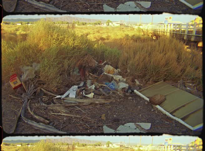 Semi truck drives past a field containing garbage during the daytime