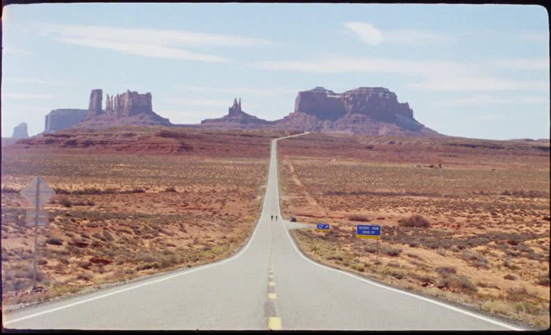 Long highway through the desert with canyons in the background