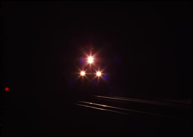 Three lights illuminate the front end of a train as it moves down the tracks at night