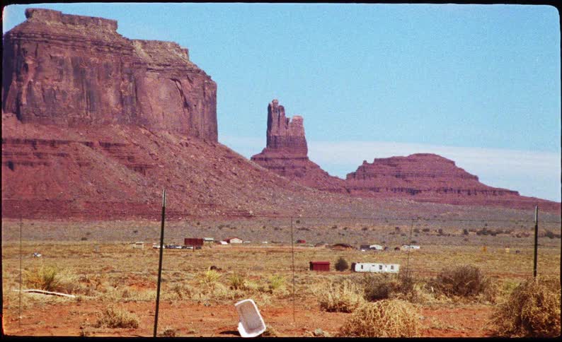 An iconic monument valley landscape at midday with a series of sparse buildings scattered across the scene