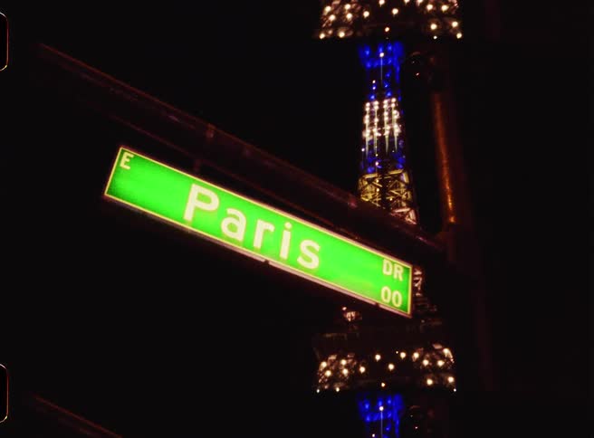Paris street sign illuminated at night with a metal structure in the background
