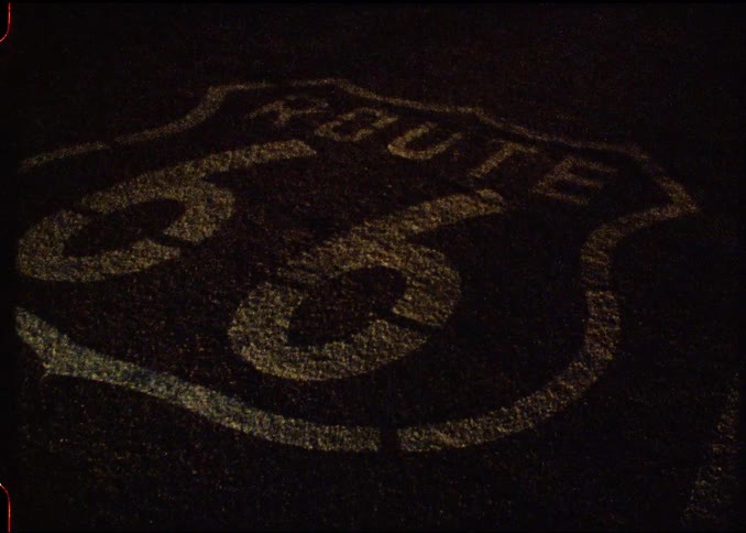 On a dark road there is a sign that says route 66 in the pavement