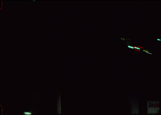 A night drive through the city with traffic lights and glowing motel and gas station signs lining the dark road