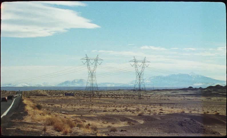 Electric transmission towers in a desert landscape with mountains in the background