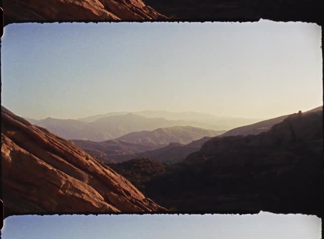 This video features a scenic view of layered mountain ranges captured with a vintage film aesthetic complete with textured borders and warm sunlight the camera slowly pans across the rugged landscape highlighting the deep shadows and golden highlights