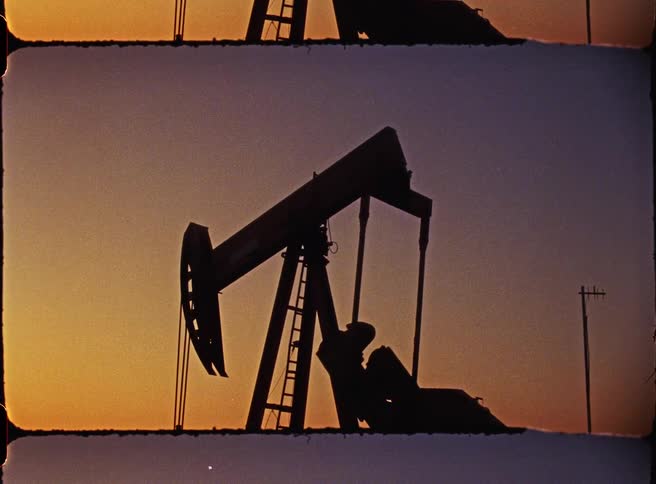 Oil pumpjack silhouetted against the evening sky with metal structure outlined by low light