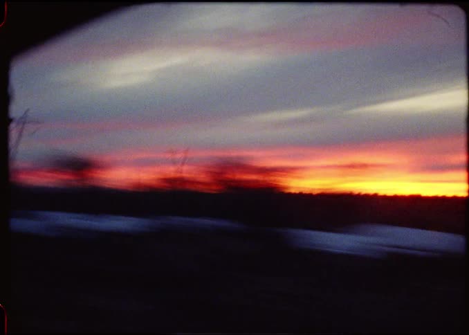 The sky is dominated by long layered horizontal bands of color near the horizon there is a brilliant glowing orange and yellow line where the sun has set above that the clouds form soft streaking lines in shades of purple grey and faded blue str