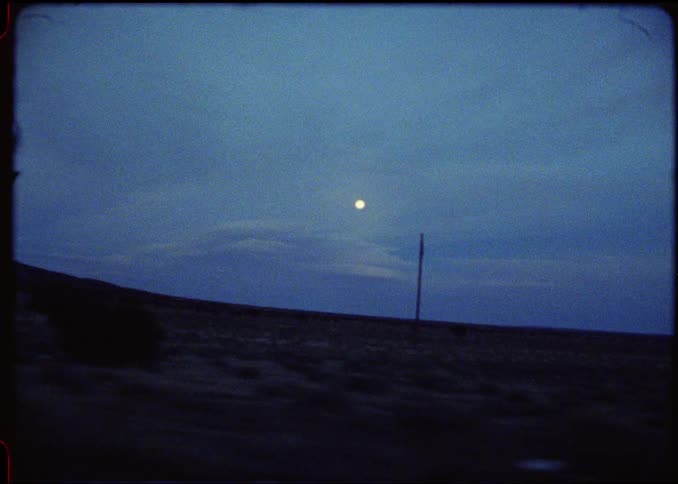 Desert area at dusk with the moon in the background against a cloudy sky