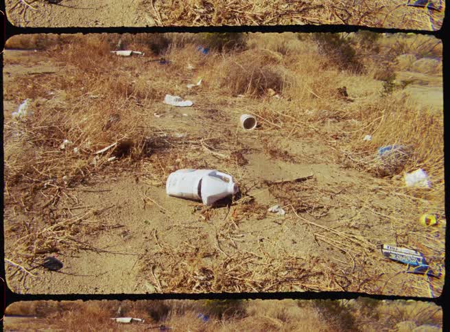 Discarded plastic jug lying among scattered trash and dry brush in a desertlike landscape
