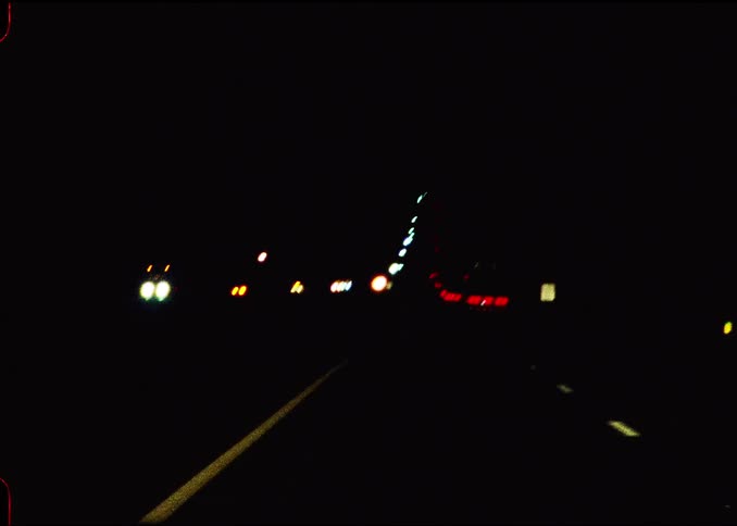 Vehicle lights on a highway at night with reflective signage in the distance