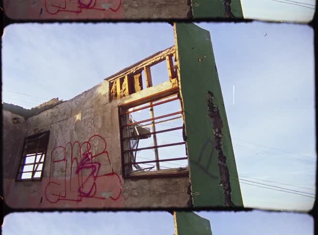 A ruined building with its roof torn away at midday featuring a series of drawings on the walls