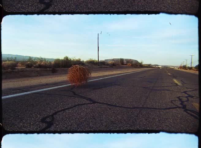 Dry tumbleweed rolls along the center of a deserted road with power poles lining the route