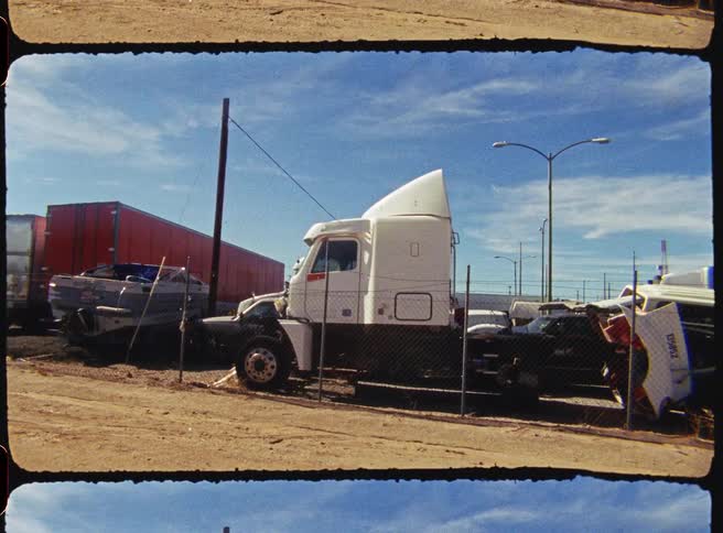 White truck parked in a fenced lot with vehicles and industrial parts
