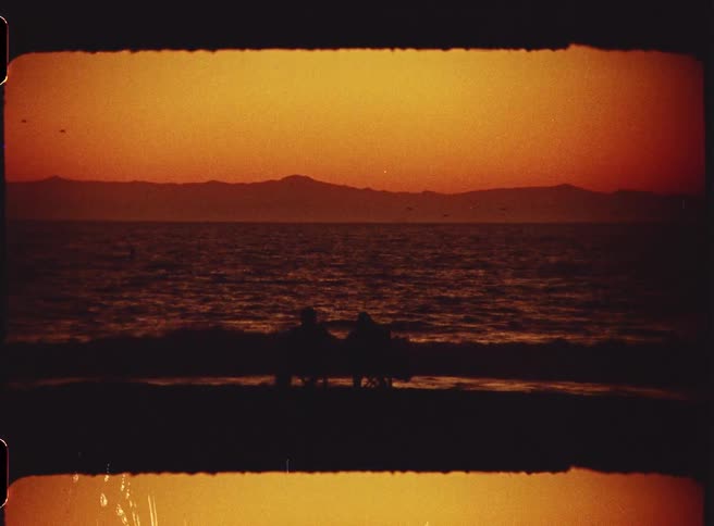 Two people sit in beach chairs on an ocean coast at sunset