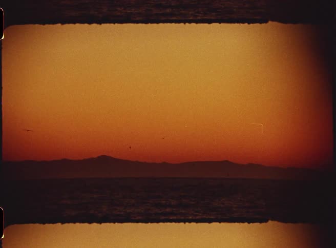 Birds flying over a valley at sunset beneath an orange sky