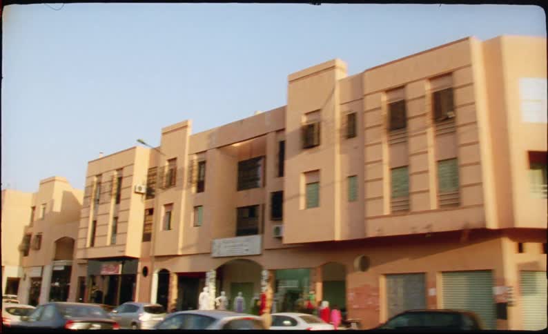 A busy city street at midday with rows of parked cars and uniformly brownpainted buildings lining both sides