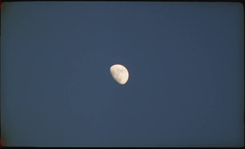 A detailed waxing gibbous moon is centered against a solid deep blue daytime sky