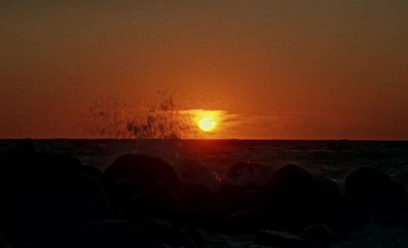 Sun partially covered in clouds over the sea near to the coast outdoors during dusk or dawn