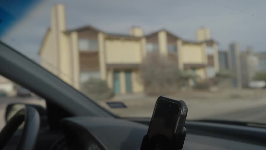 Phone mounted on a car dashboard holder with an urban street blurred in the background