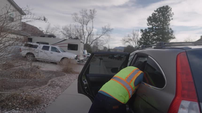 Young man gets out of his car parked on the street and takes a package from the back seat then walks down the sidewalk