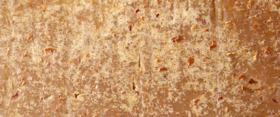 This video features a highdefinition macro shot of a dense textured surface with earthy amber and tan tones it showcases a complex material filled with organic specks and fine vertical cracks suggesting a substance like artisanal soap or compressed na