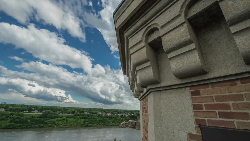 A building by the water has clouds passing by