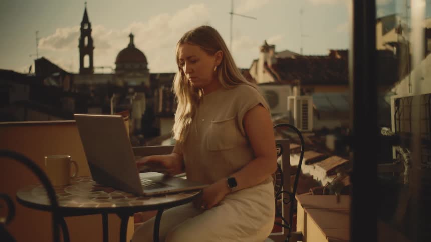 The woman is typing on her laptop on the balcony