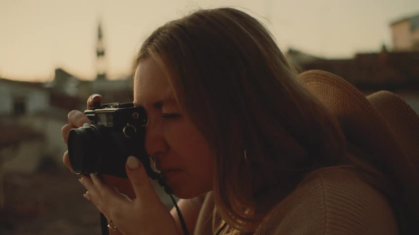Young woman holds her camera and leans forward as she adjusts the lens and takes a picture