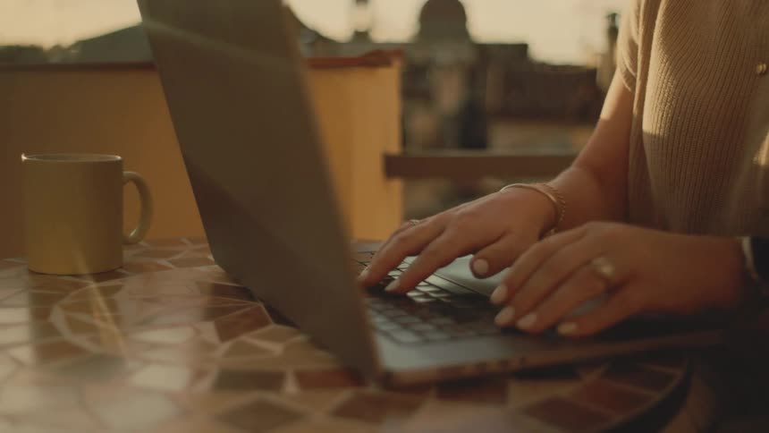 Woman sitting at an outdoor table typing on a laptop computer