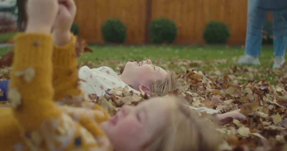 Children lie on a lawn covered with dry leaves in a residential backyard