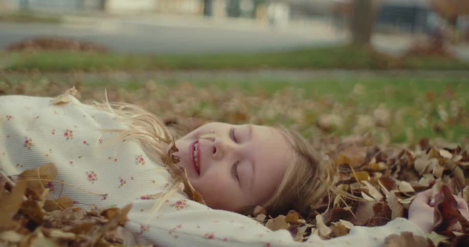 Young girl lying in the leaves in her front yard and laughing