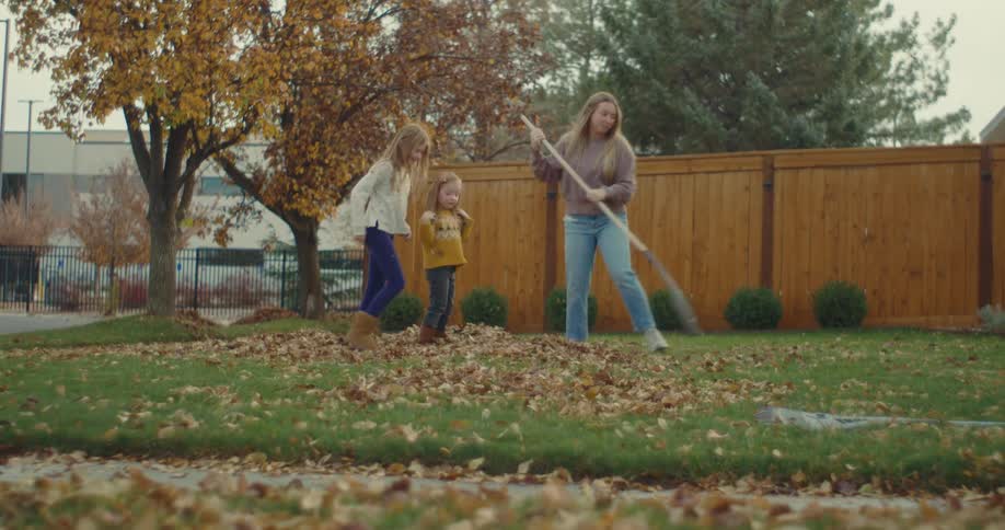 Woman rakes dry leaves while children play in the backyard