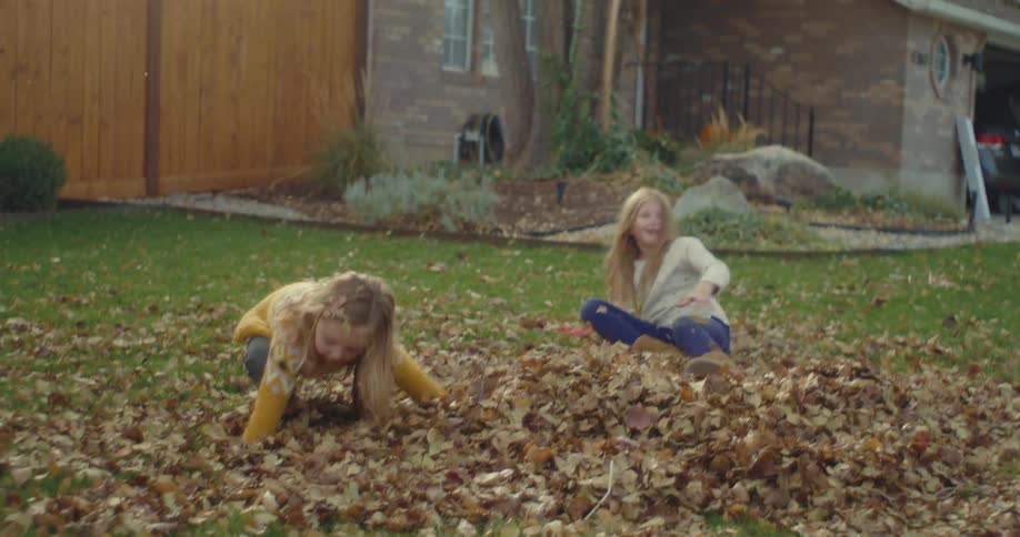 Children play in a backyard tossing dry leaves into the air in front of a residential house