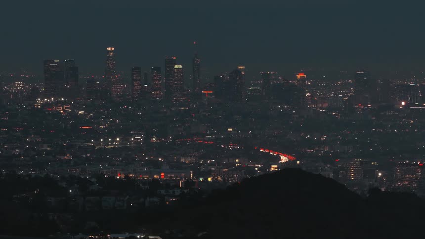 Nighttime urban landscape with illuminated skyscrapers and continuous vehicle flow on the roads below