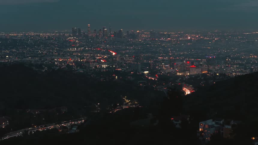 Panoramic urban view at dusk with illuminated buildings and highways forming light trails