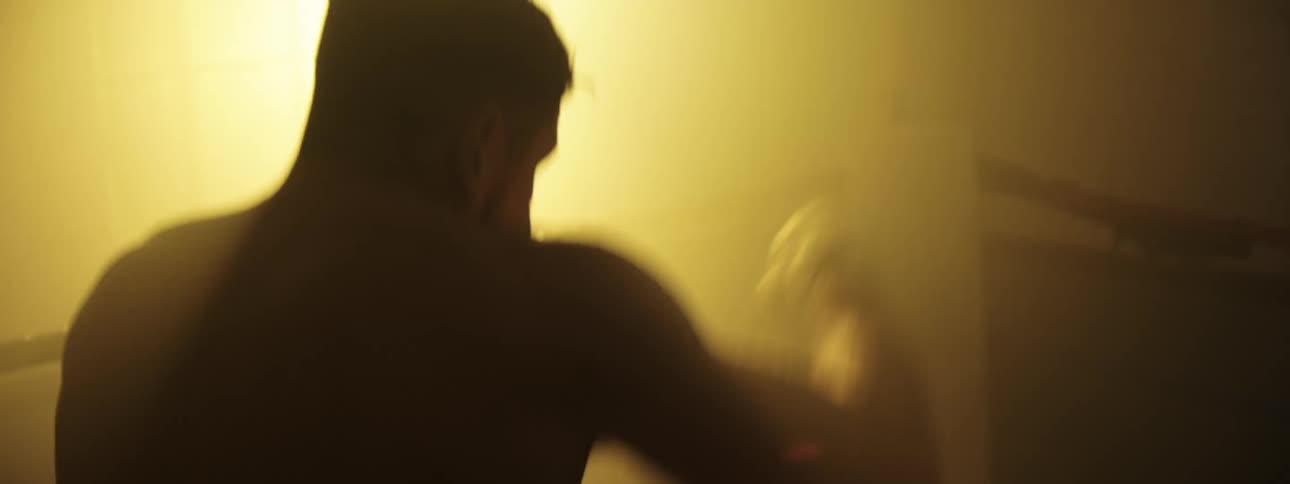 Boxer in silhouette with wrapped hands near the face backlit in an indoor setting