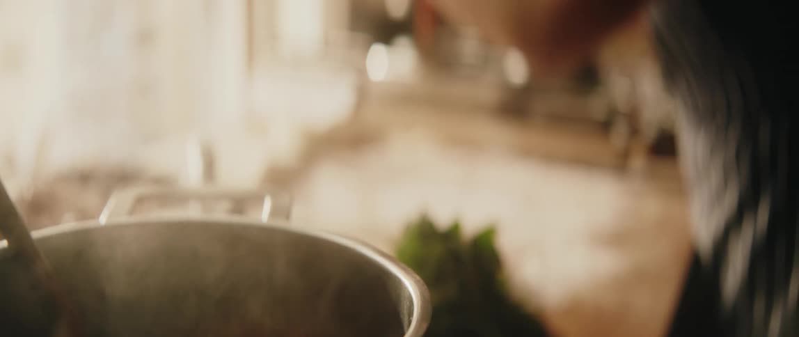 Person preparing food in a kitchen with a steaming pot on the stove and hands chopping ingredients on the counter