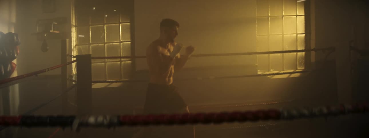 Boxer trains movements inside a ring lit by natural light