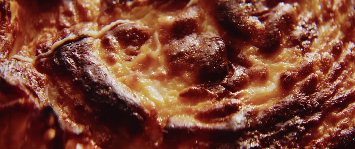 An extreme closeup shot shows the goldenbrown caramelized surface of a baked dish such as a basque cheesecake or custard with a deeply textured and slightly charred top