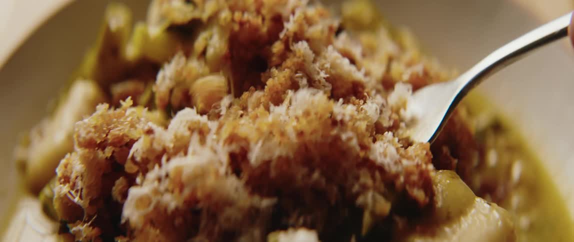 A close view shows a prepared dish of green vegetables topped with golden brown breadcrumbs and grated cheese in a white bowl