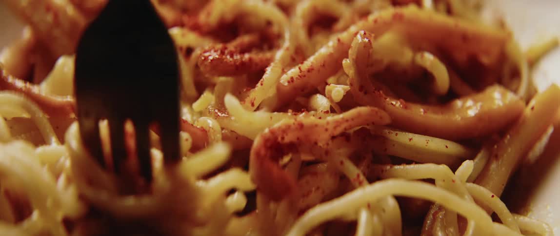 Metal fork twirling pasta from a dish indoors
