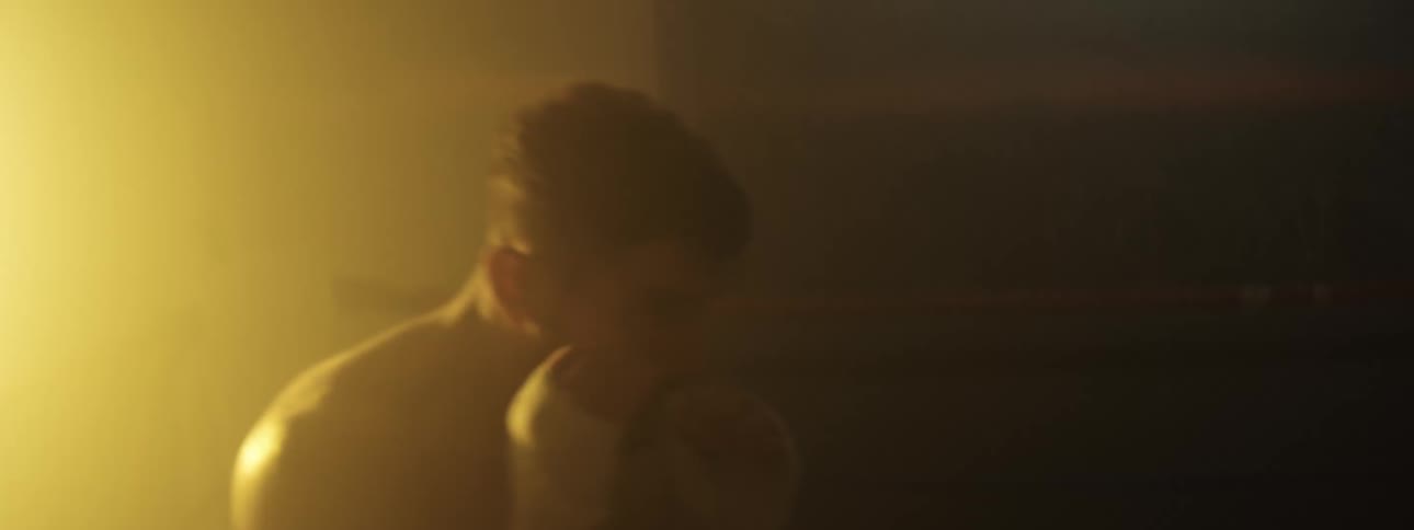 Boxer training punches with a defensive stance under low lighting in an indoor setting