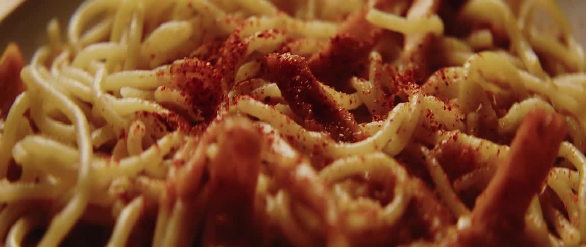 Spaghetti dish sprinkled with red seasoning on a dish indoors