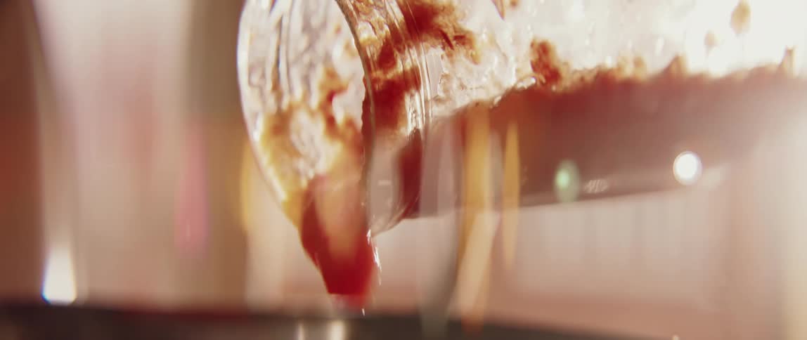Sauce being poured from a glass container into a heated pot on the stove