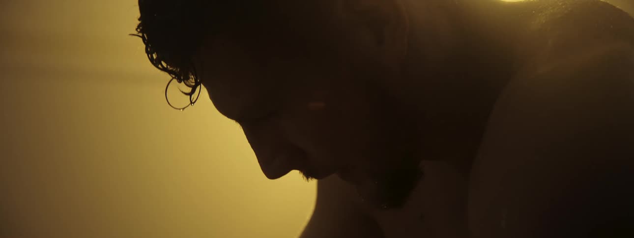 A sweaty mans face in profile as he breathes heavily in a warm hazy light