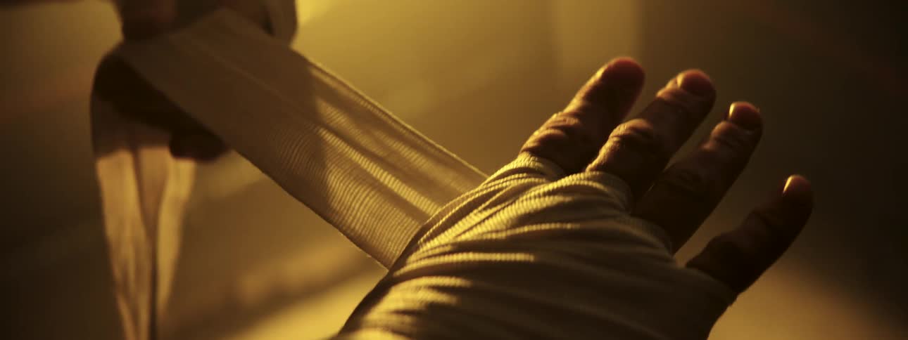 A person wraps their hands with boxing wraps in a dimly lit hazy room